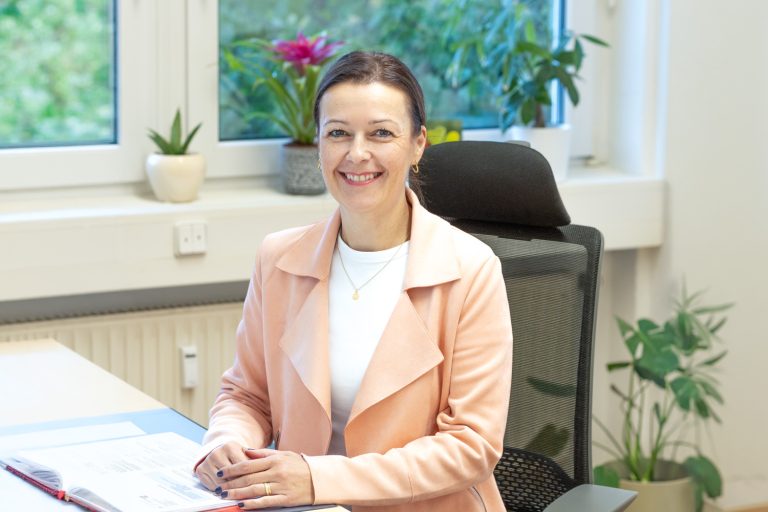 Eine lächelnde Frau sitzt an einem Schreibtisch in einem Büro.